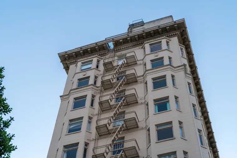 Pre-war brick walk-up building with fire escapes and a flat roof behind a parapet